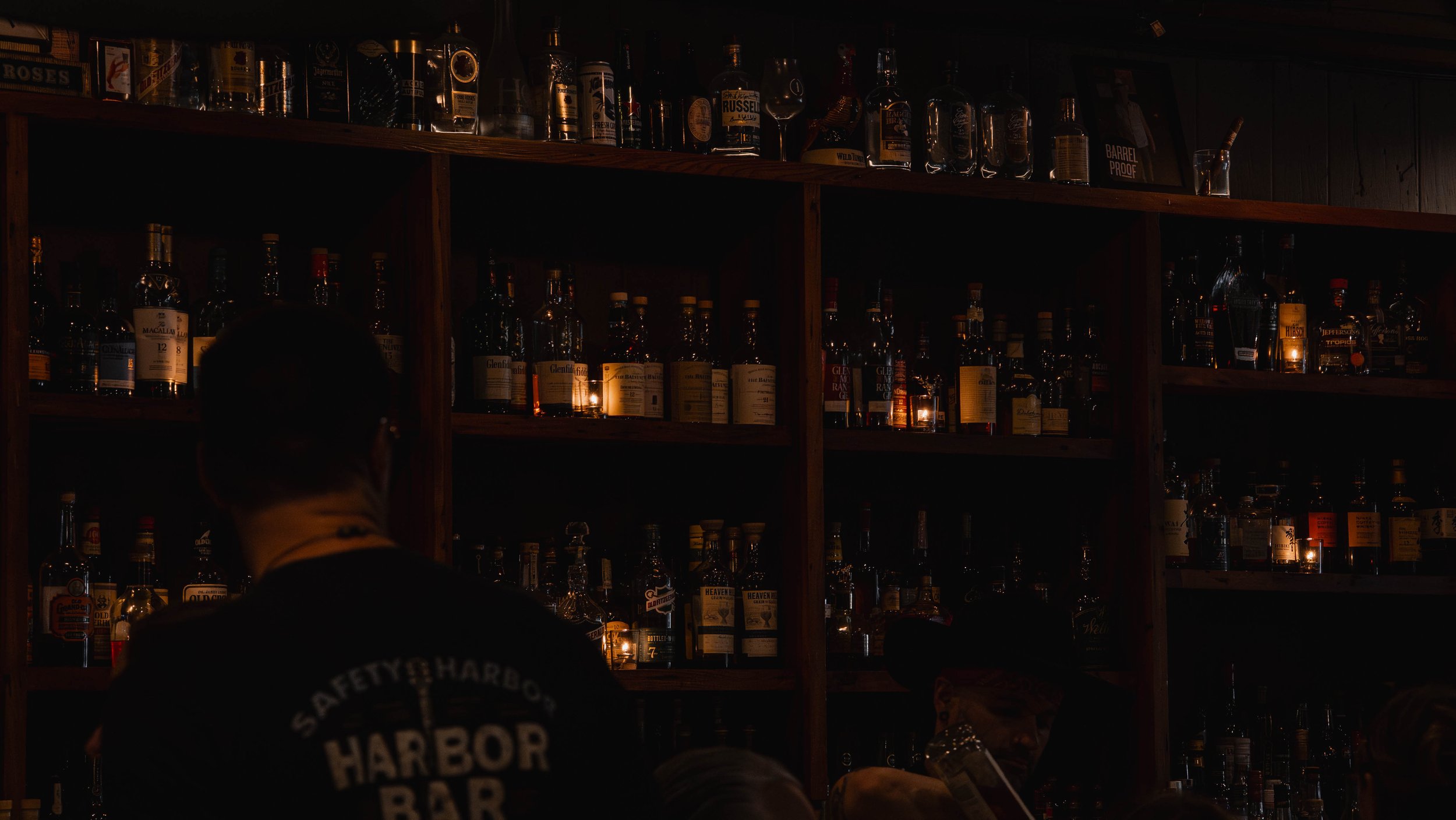 Bar with shelves filled with various bottles of alcohol in a dimly lit setting.