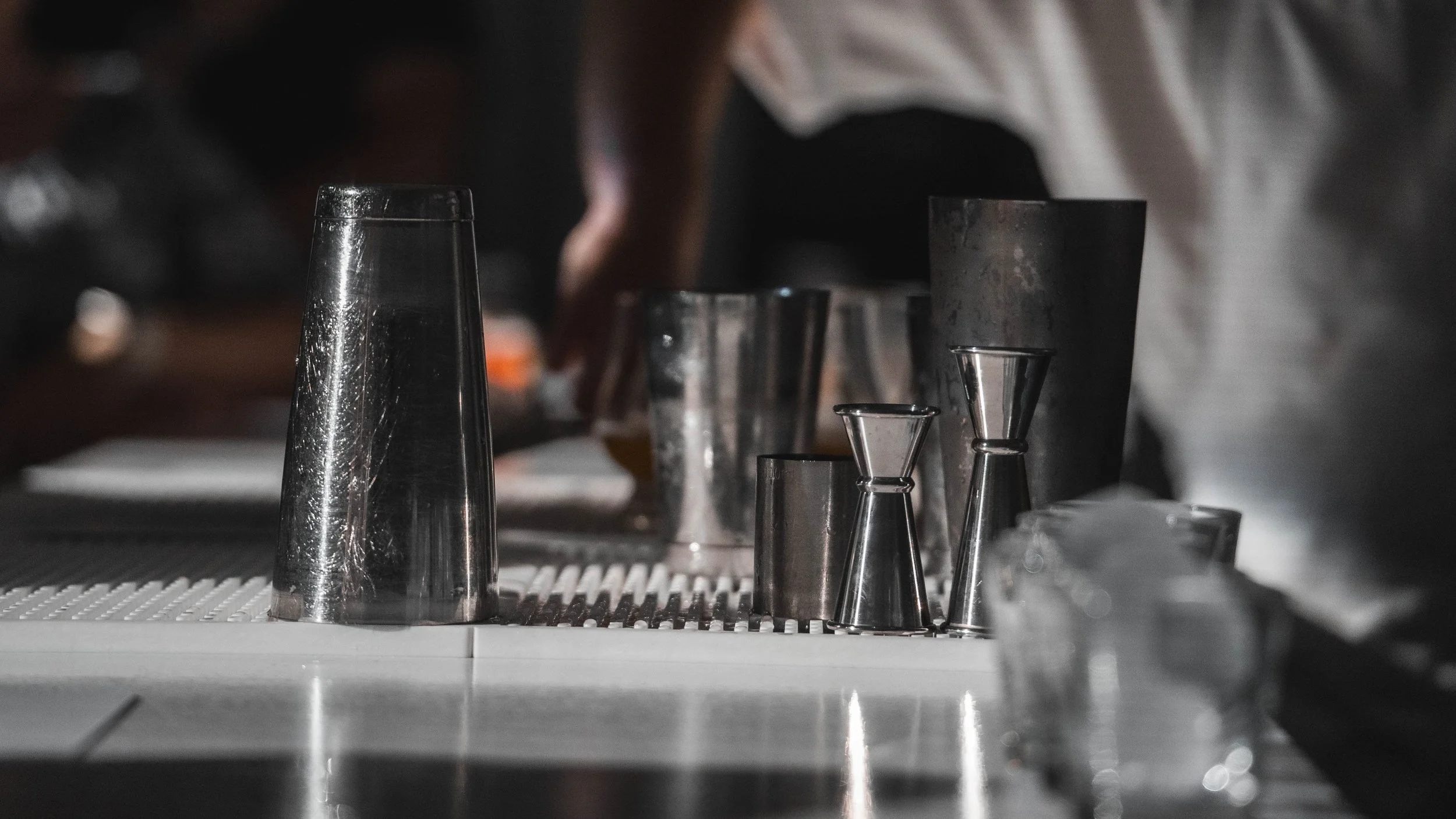 Various stainless steel jiggers and metal measuring tools arranged on a surface, with some objects in focus and others blurred in the background.