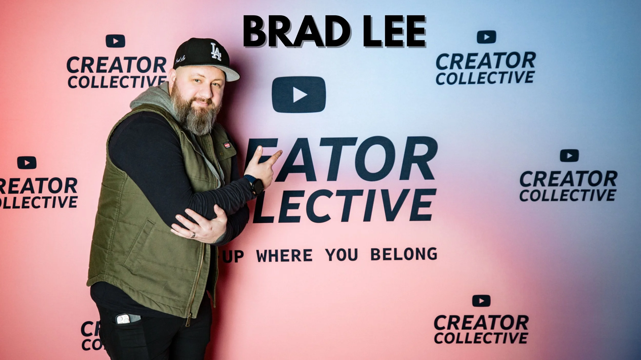 Brad Lee founder of Lee Fragrances standing with a beard and wearing a LA baseball cap pointing at a large poster that reads "Brad Lee" and "Creator Collective" in black text, with a pink and blue gradient background.