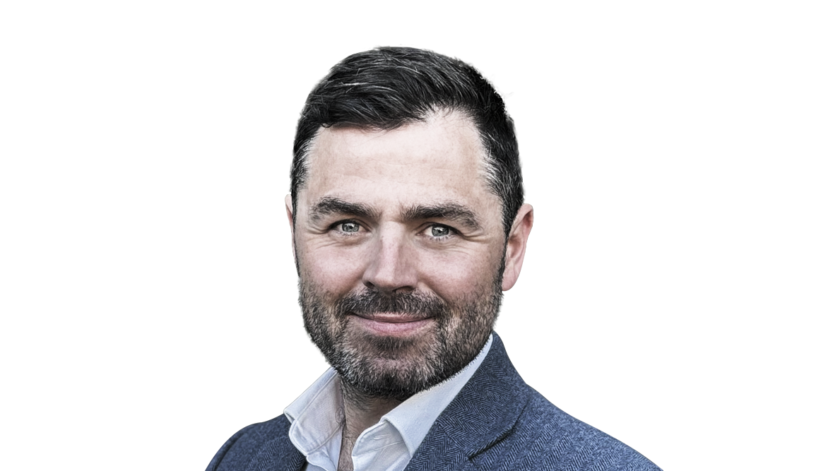 A portrait of a smiling man with dark hair, trimmed beard, wearing a suit jacket over a white shirt