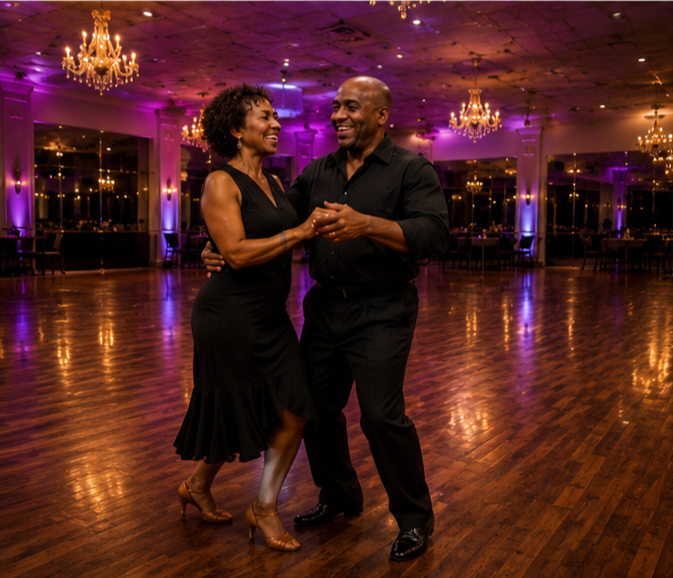A happy couple dancing together in a dimly lit ballroom with purple lighting and chandeliers.