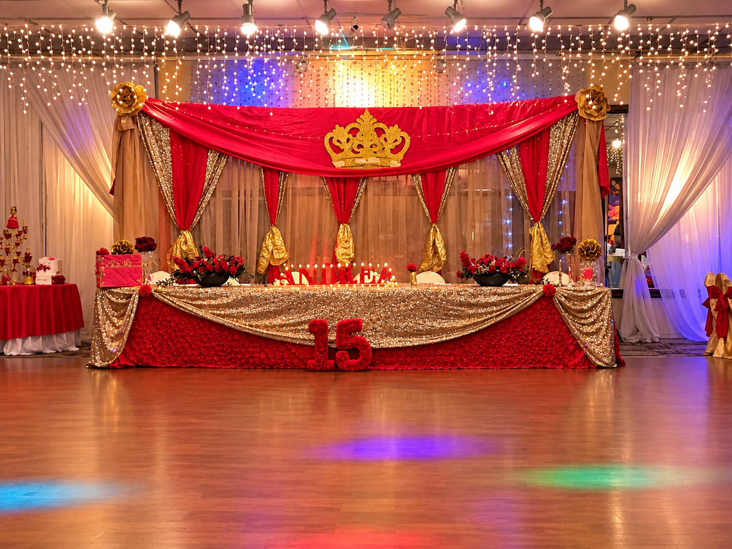 Decorated banquet table with red and gold drapery, floral arrangements, and a crown emblem at a 15th birthday celebration with the number 15 displayed.