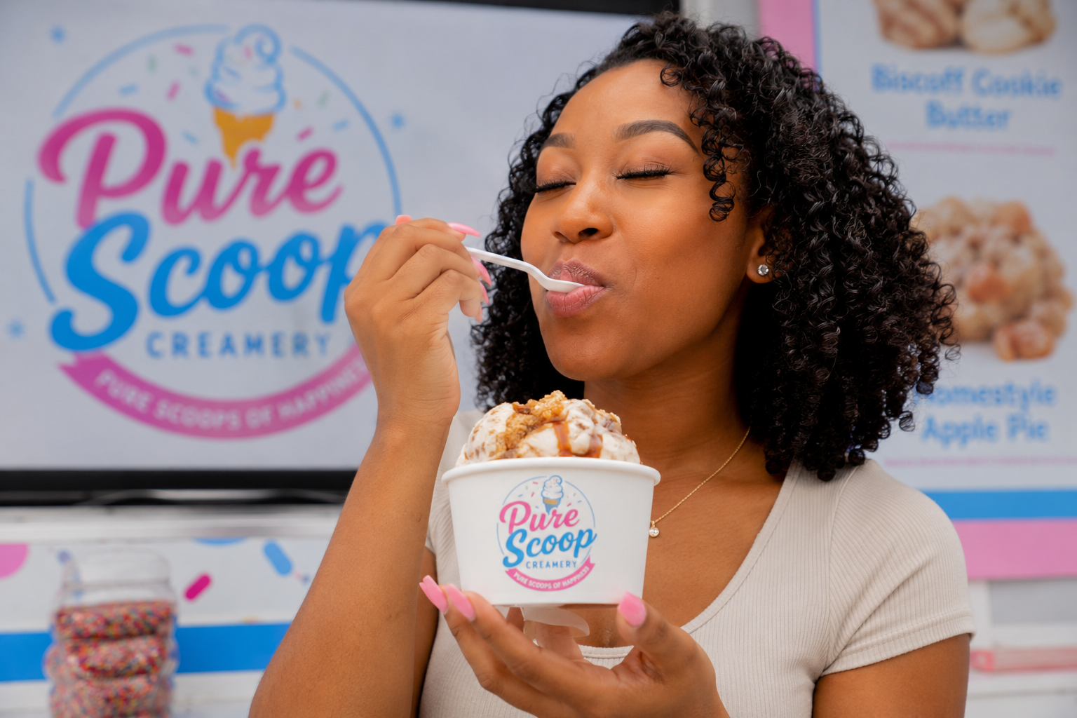 Woman with curly hair enjoying a cup of ice cream with a spoon at Pure Scoop Creamery.
