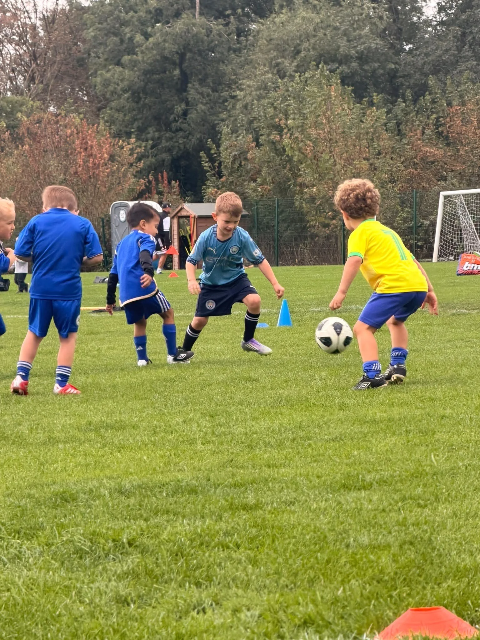 Children playing soccer on a field during daytime with trees in the background.