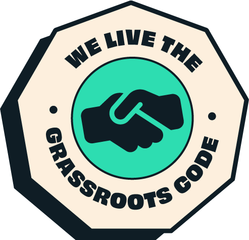 A circular badge with a handshake icon in the center, and the text "We Live the Grassroots Code" around it.