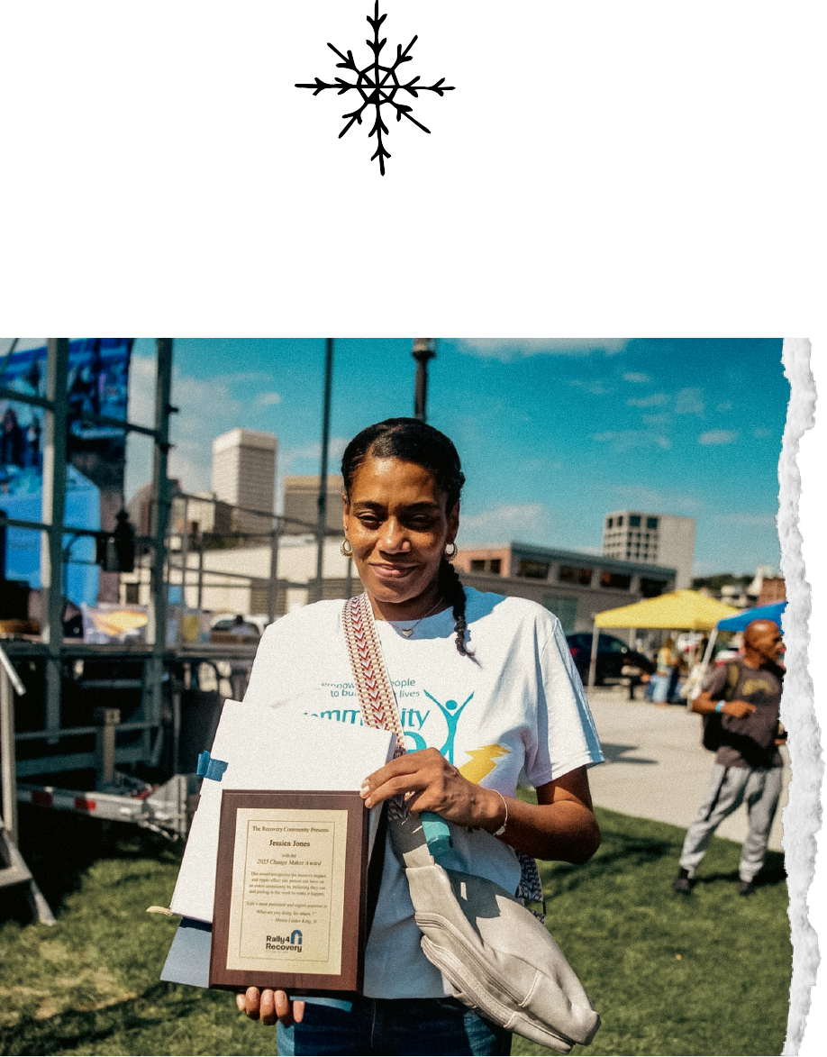 Woman holding a framed award at an outdoor event with tents and people in the background.