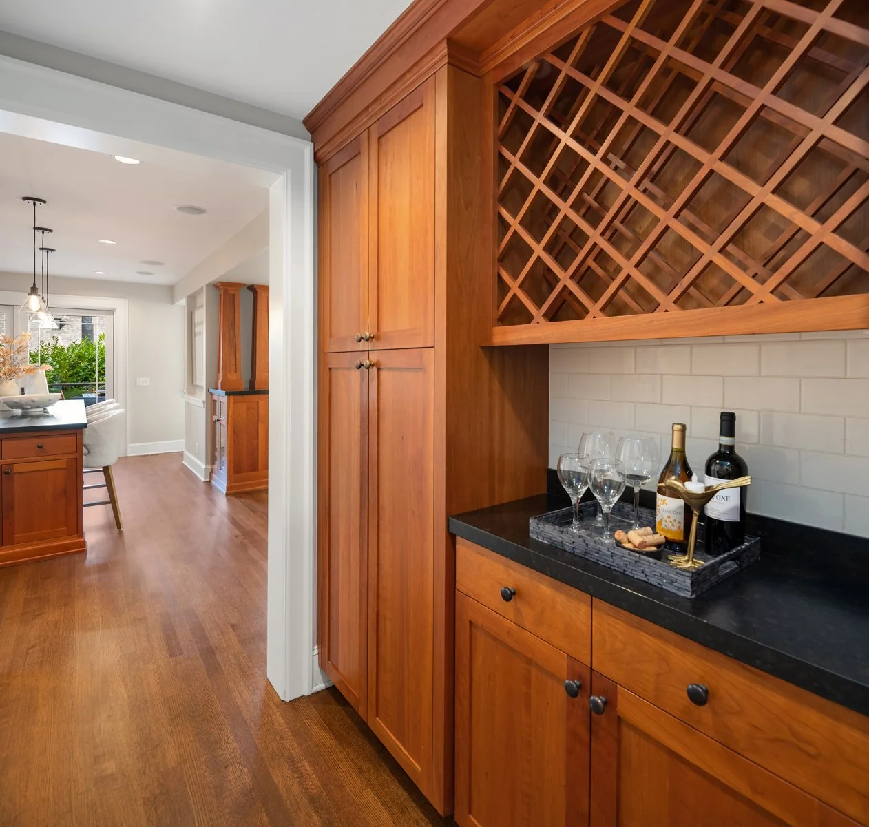 Kitchen with wooden cabinets, black countertop, wine bottles, glasses, and wine corks on a tray.