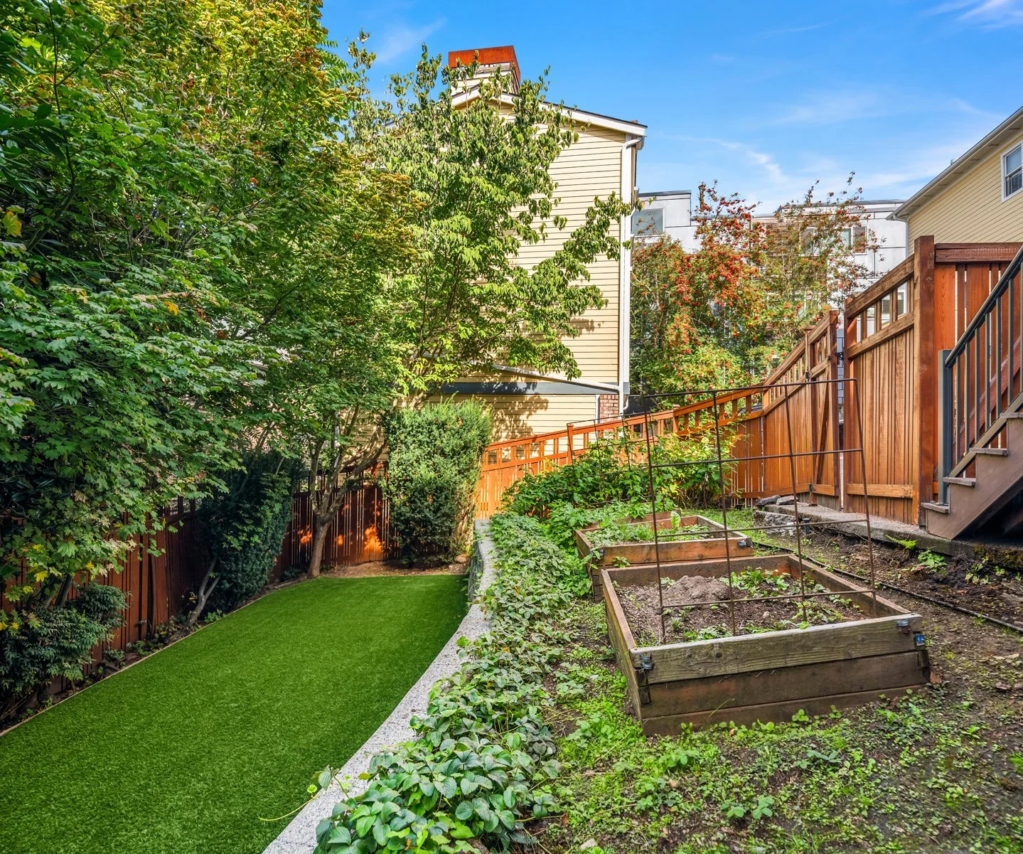 Backyard garden with lush green trees, a well-maintained grass area, and garden beds with some plants.