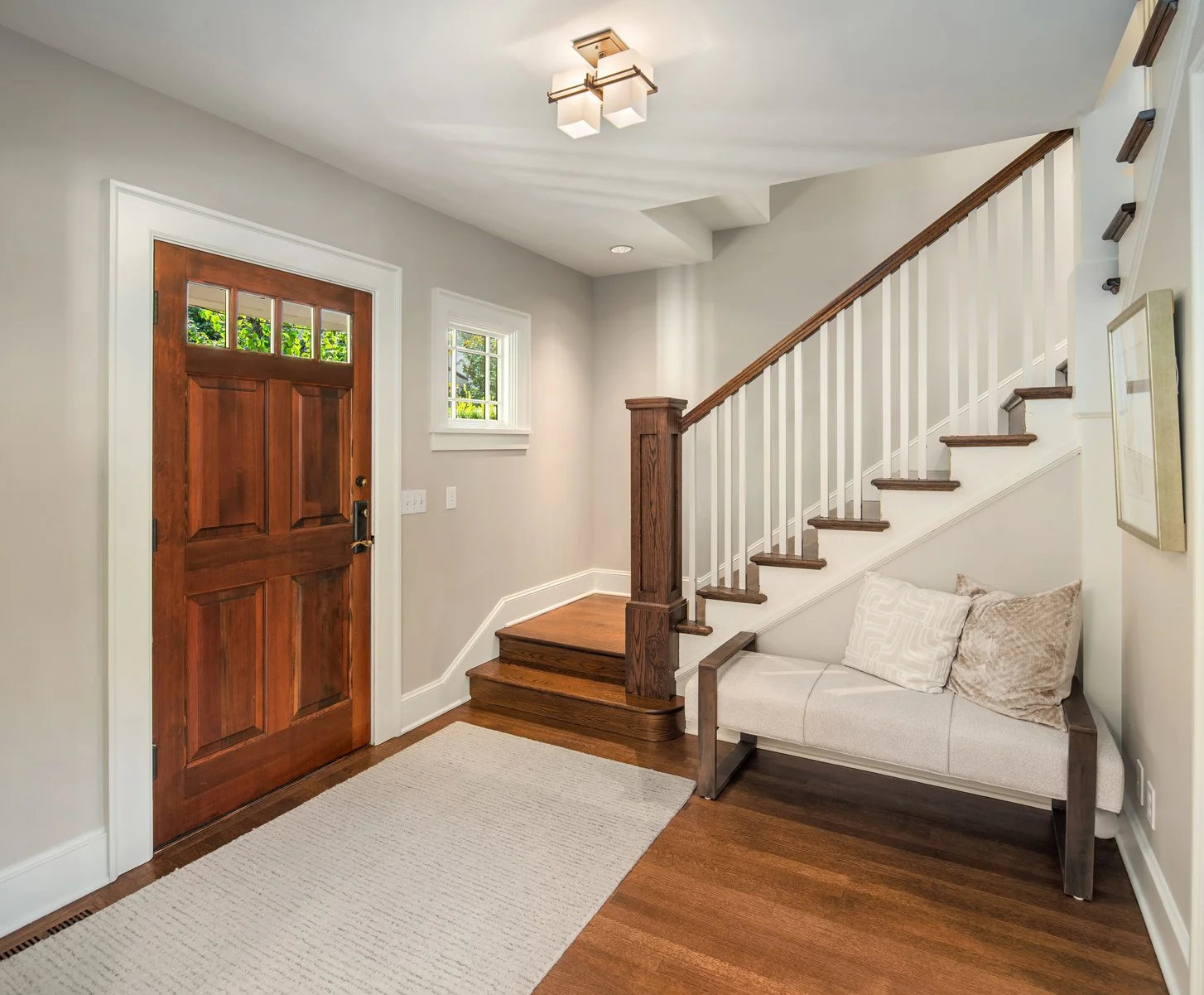  entryway with wooden door, small window, staircase, and a bench with pillows.