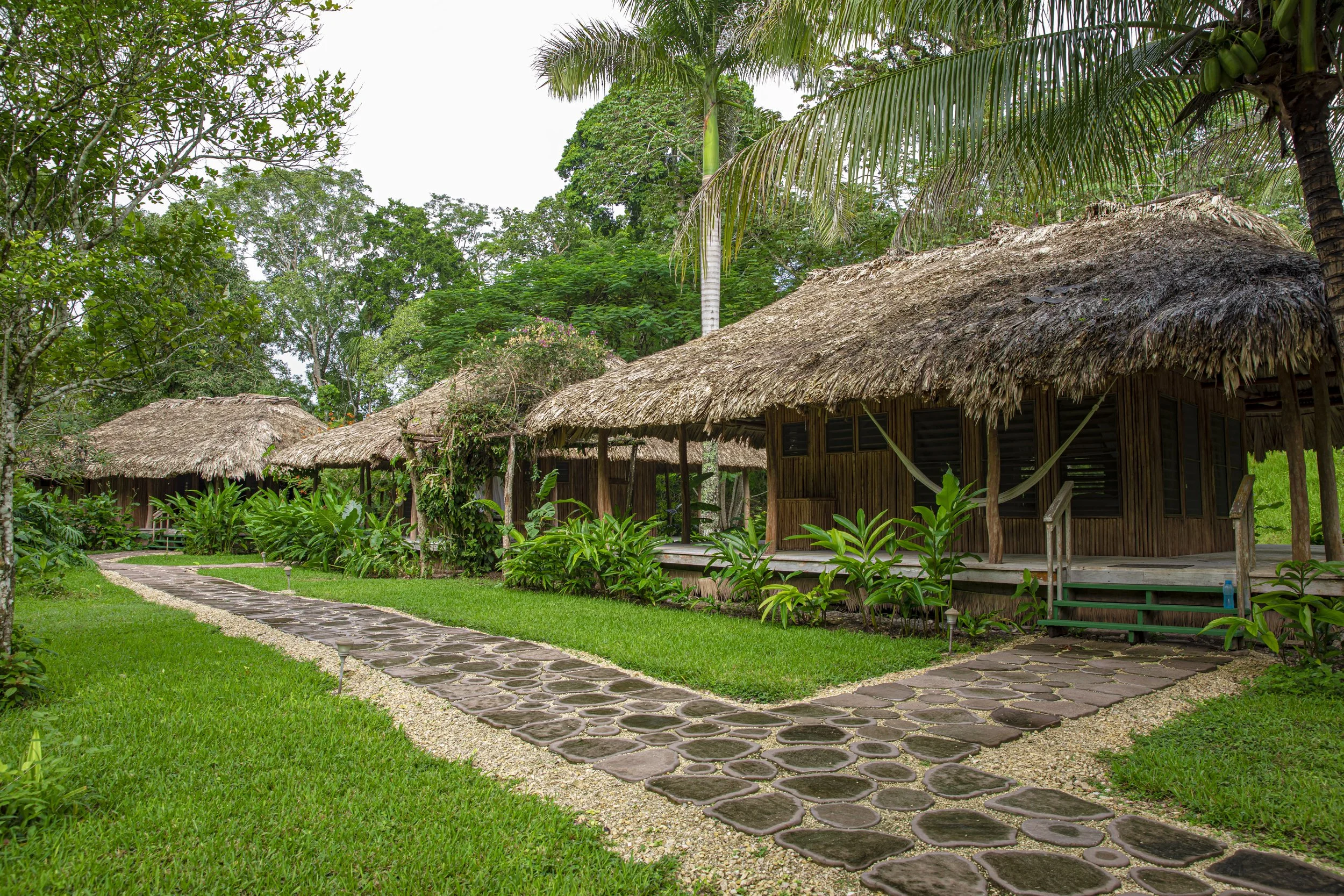 Thatched cabanas among trees, with a stone path curving across a mown lawn