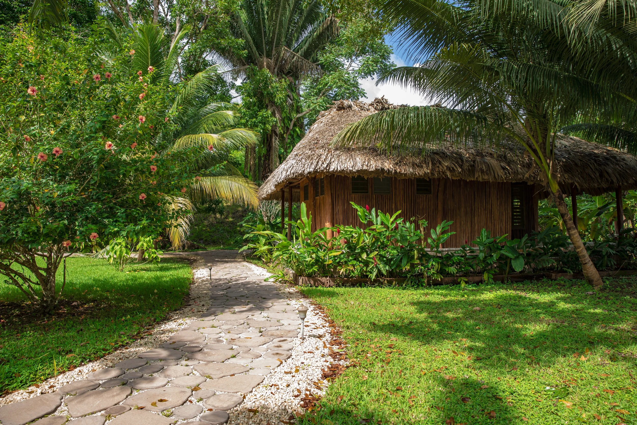 Stone path through a flowering garden to a thatched-roof cabana