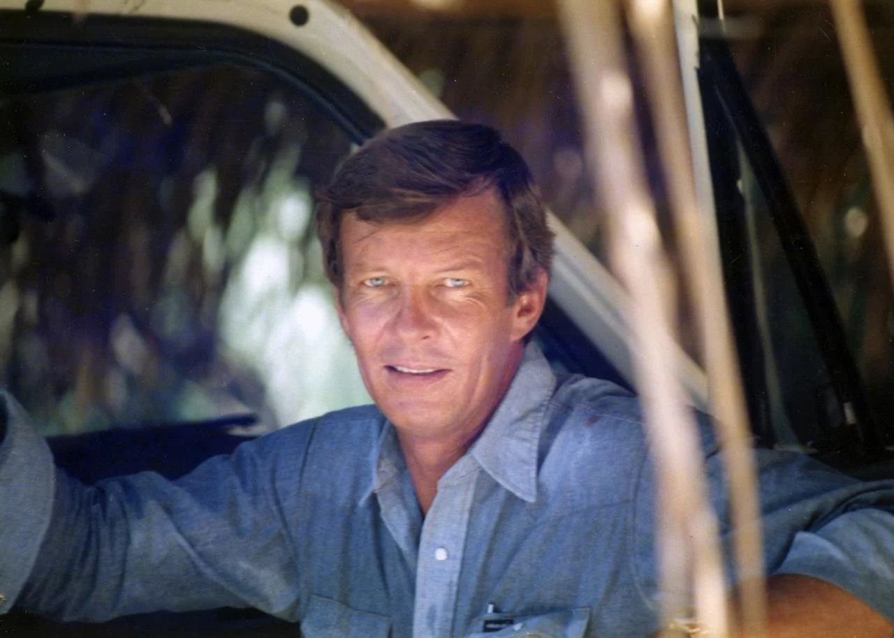 A smiling man in a light blue shirt at the wheel of a vehicle