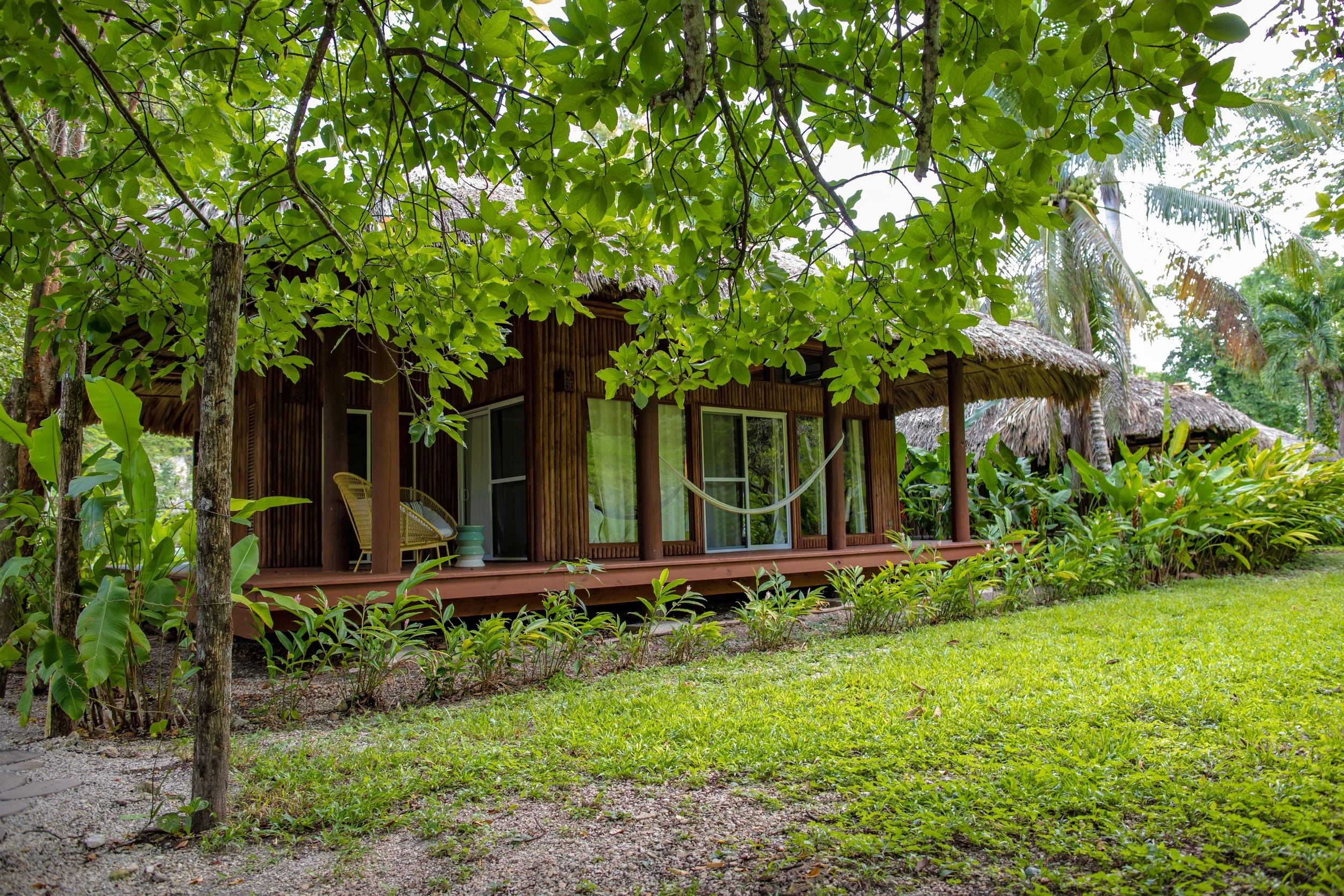 Wooden cabana with a long veranda, set among large trees and lawn