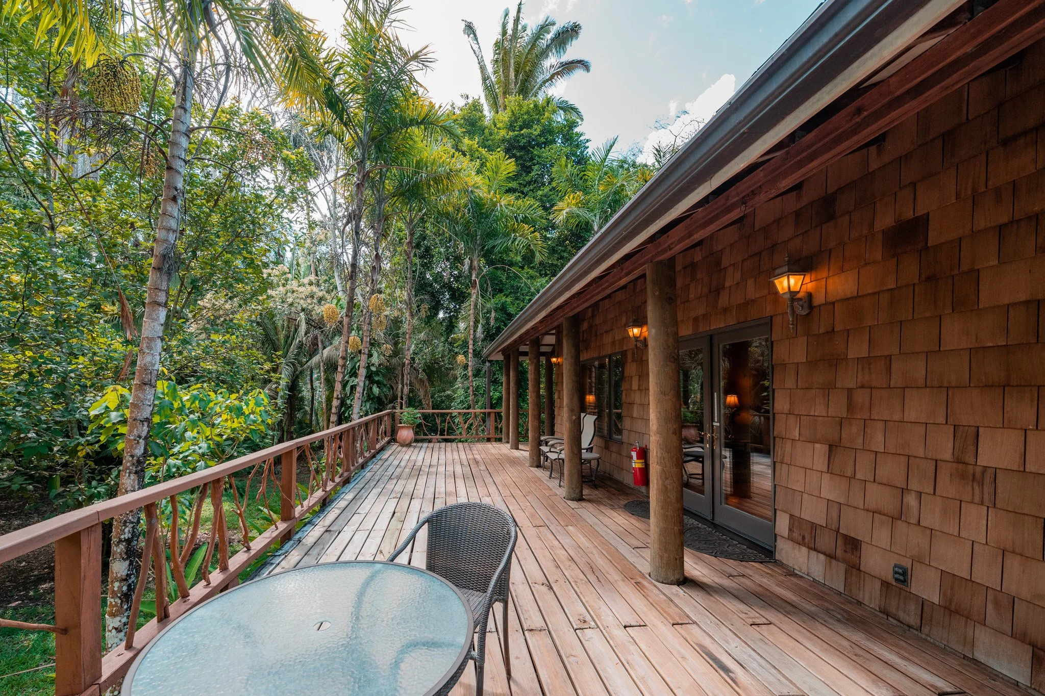 Wooden deck with a glass-top table and chairs beside a wooden house among tall trees