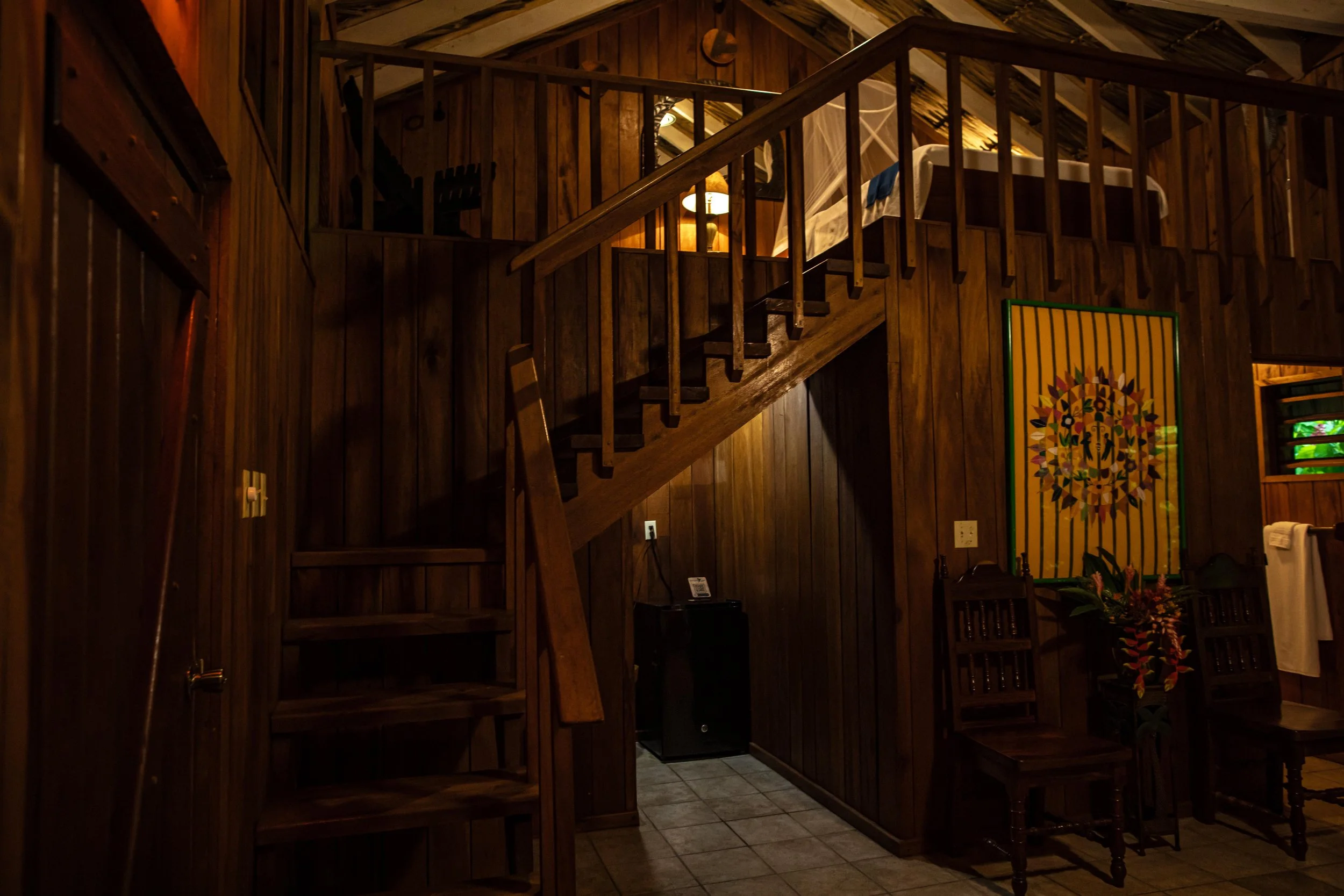 Wood-paneled room with a staircase, a dining table and chairs, colorful artwork and flowers in warm light