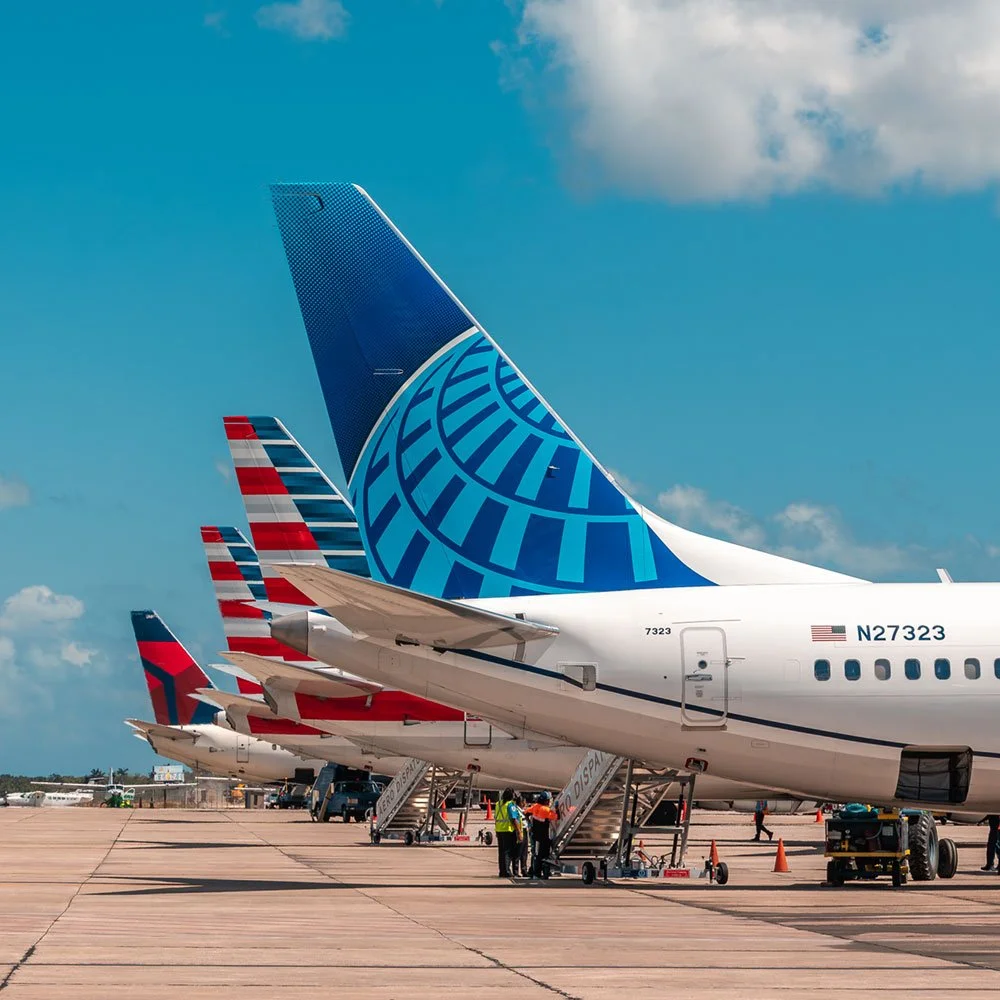 Multiple airplanes parked at an airport gate with stairs and ground crew working under a partly cloudy sky.