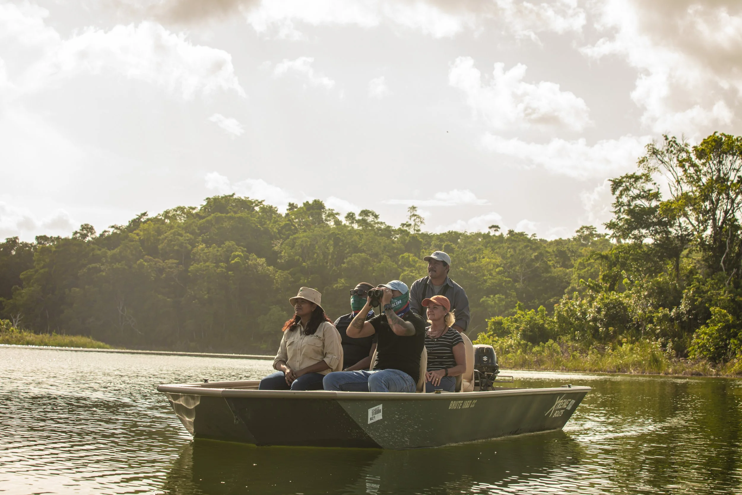 Guests in a flat-bottomed boat on a calm lagoon, with rainforest along the shore