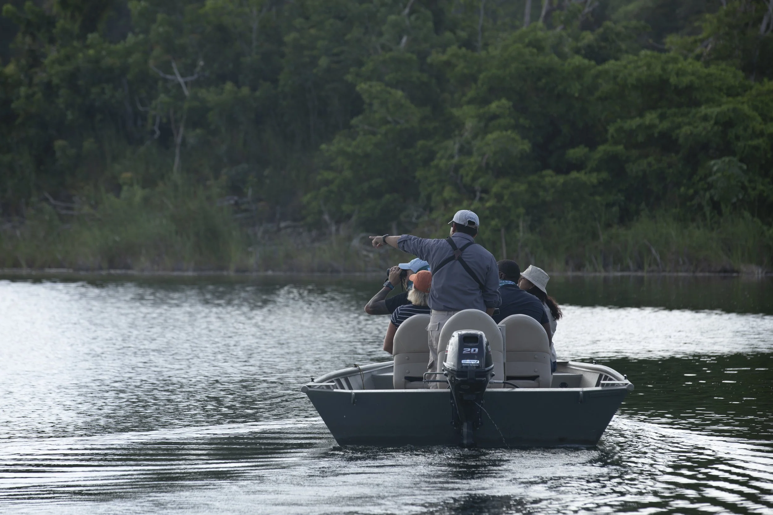 Guests in a small motorboat heading across calm water toward dense rainforest