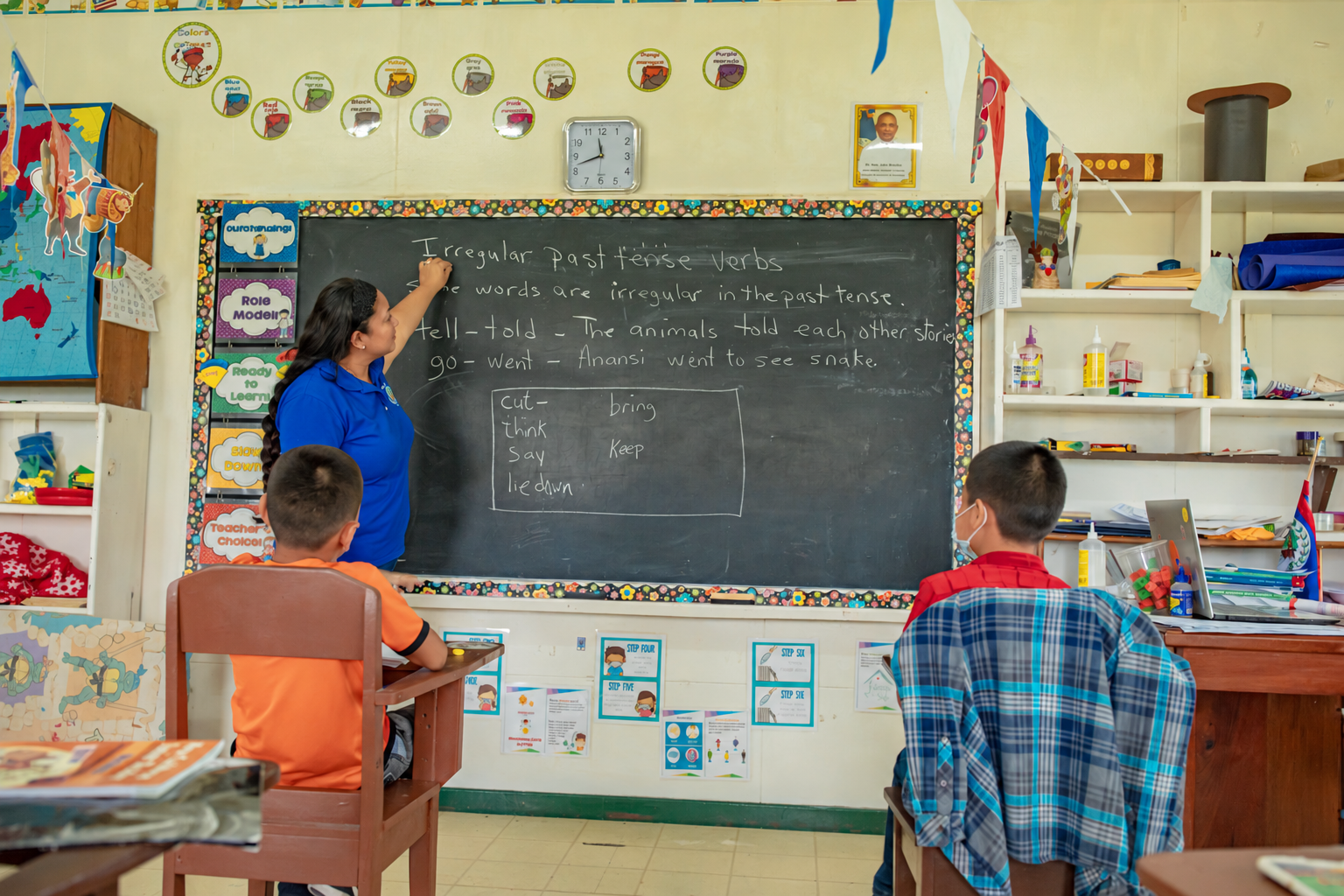 A teacher writing a lesson on a blackboard while two students sit at their desks