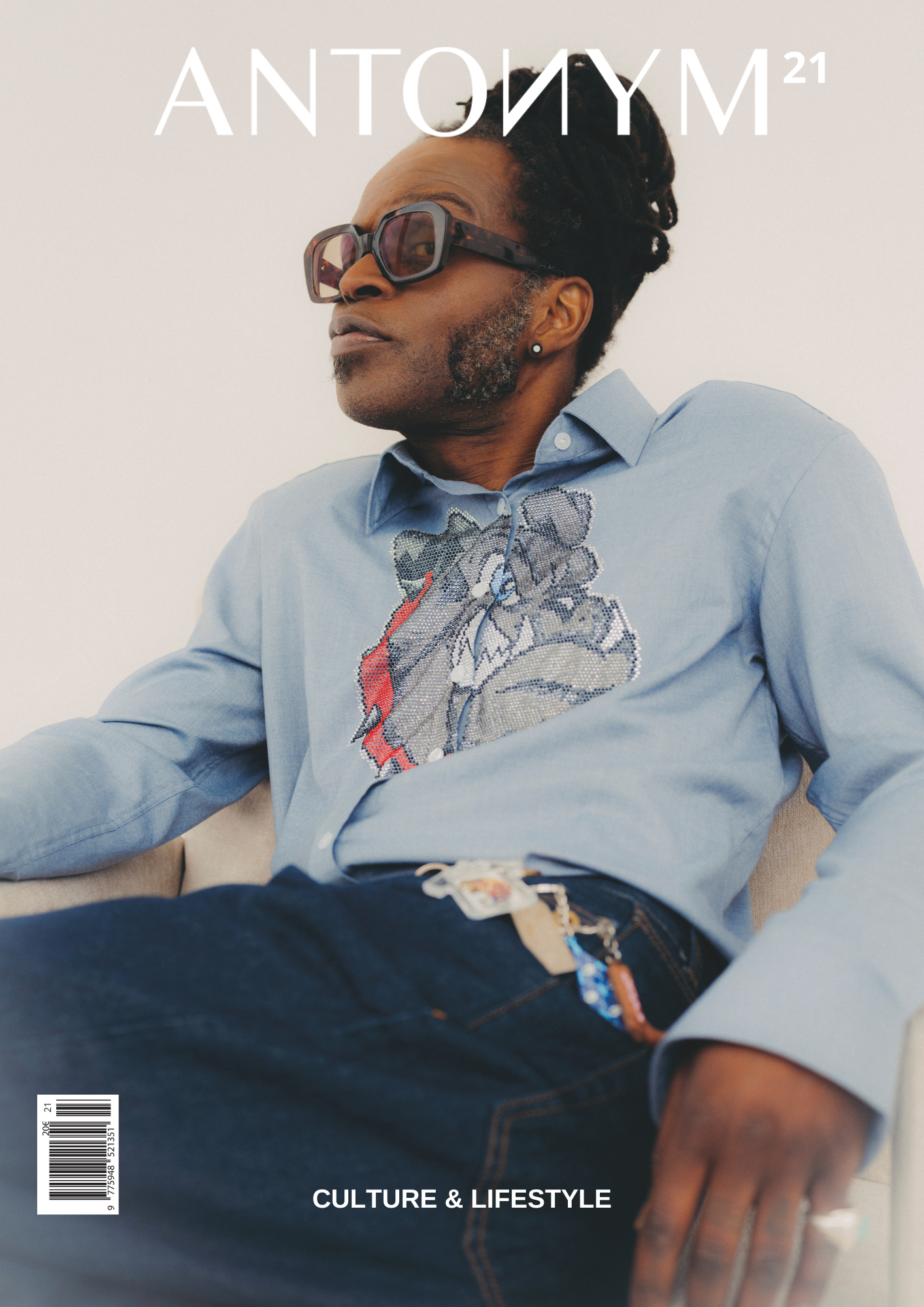 Une personne élégante avec des lunettes de soleil et une chemise bleu clair, assise sur un canapé, avec un fond blanc, sur la couverture d'un magazine intitulé 'Antonym 21' avec le thème 'Culture & Lifestyle'.