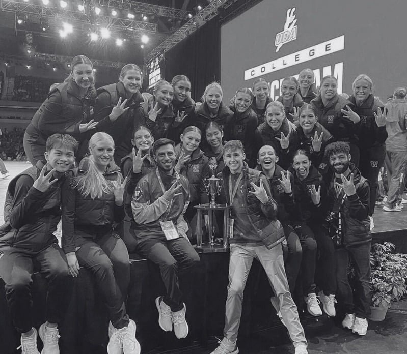 A group of female athletes in athletic gear posing with a trophy, celebrating their victory at an indoor sports event.