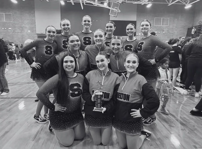 Girls cheerleading team posing in a gym with one member holding a trophy.
