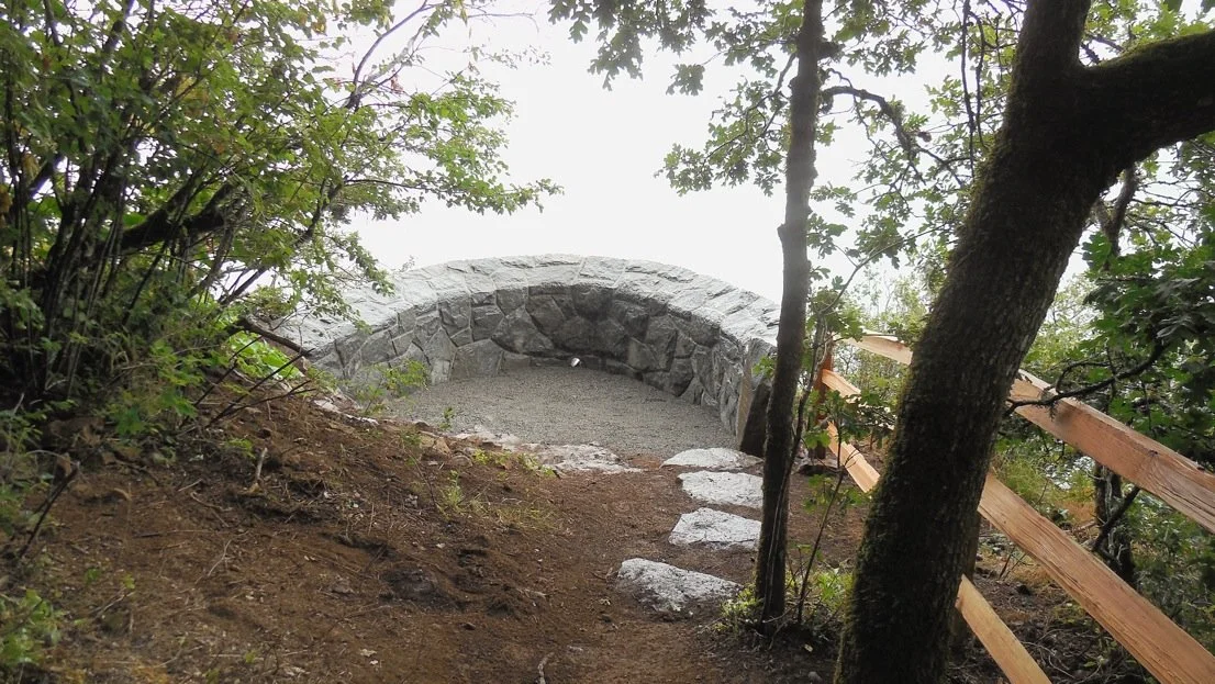 A stone footbridge over a dirt trail in a wooded area.