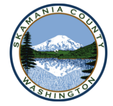 Seal of Skamania County, Washington, featuring Mount St. Helens and a lake with reflections, surrounded by trees.