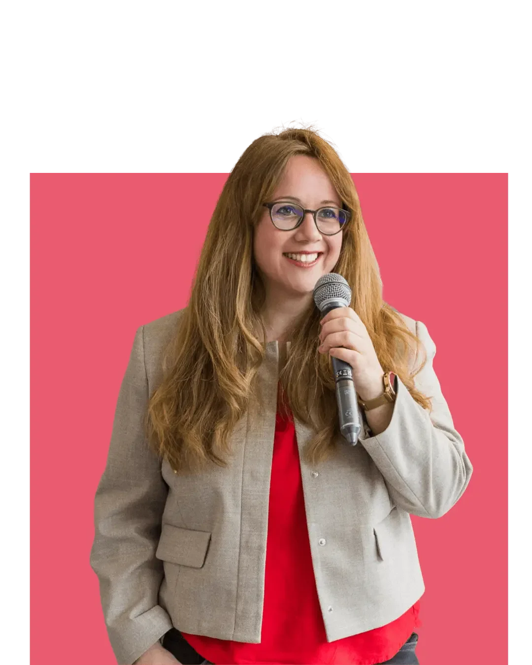 Eine lächelnde Frau mit Brille hält ein Mikrofon, vor einem pinken Hintergrund.