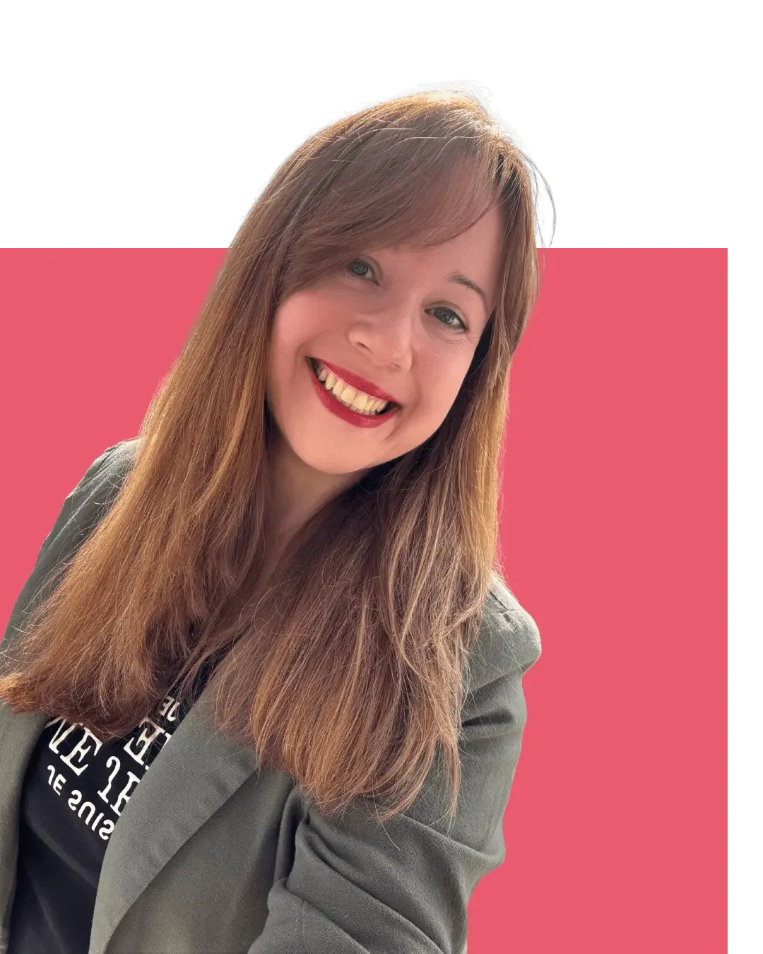 Ein Frauenporträt mit langen braunen Haaren, rotem Lippenstift, lachend, trägt eine graue Jacke und ein schwarzes T-Shirt, vor einem rosa Hintergrund.
