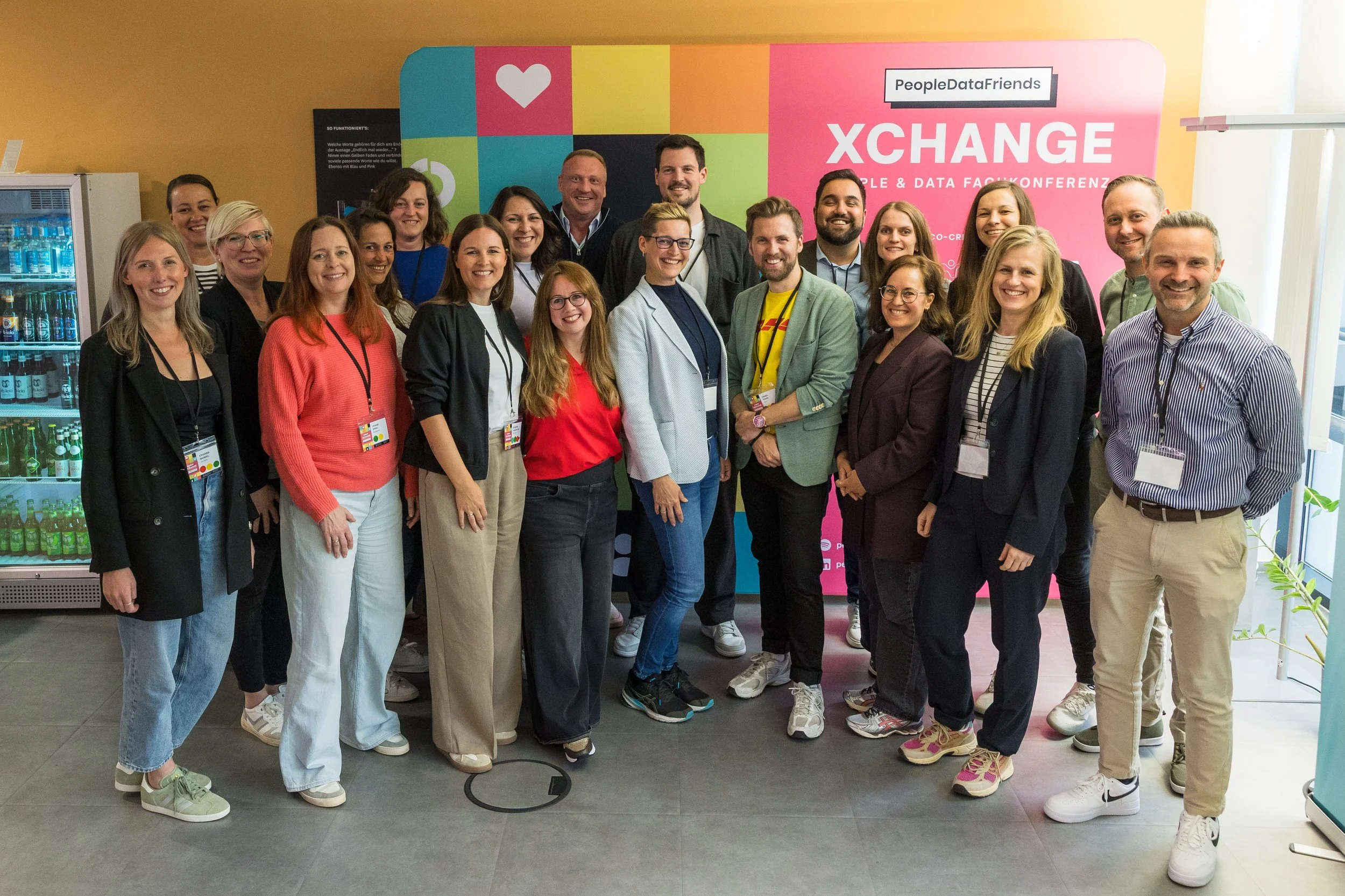 Gruppe von Menschen steht zusammen vor einem bunten Hintergrund mit dem Text 'XCHANGE' und 'People & Data Fachkonferenz'.