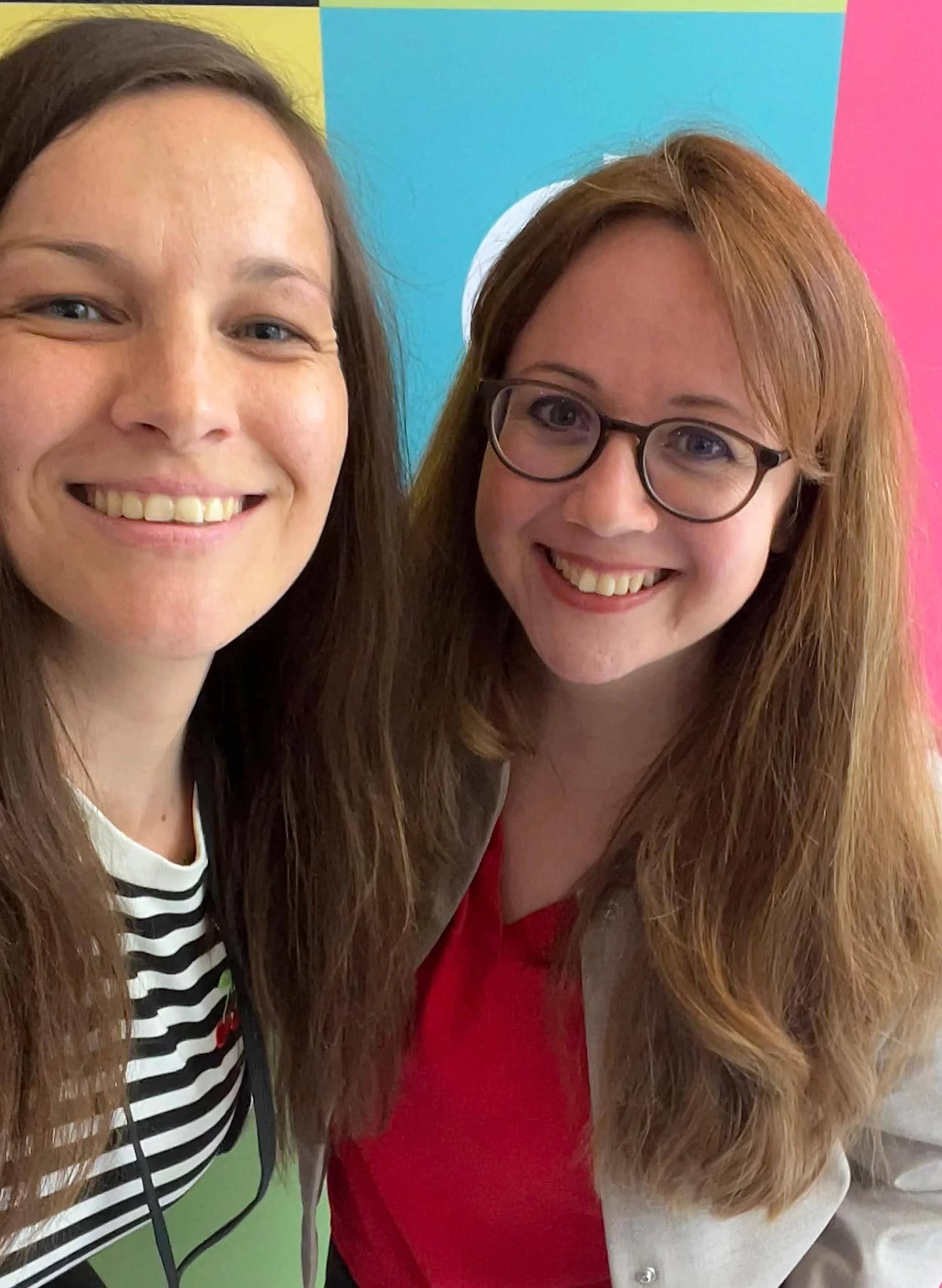 Zwei lachende Frauen in engem selfie vor buntem Hintergrund.