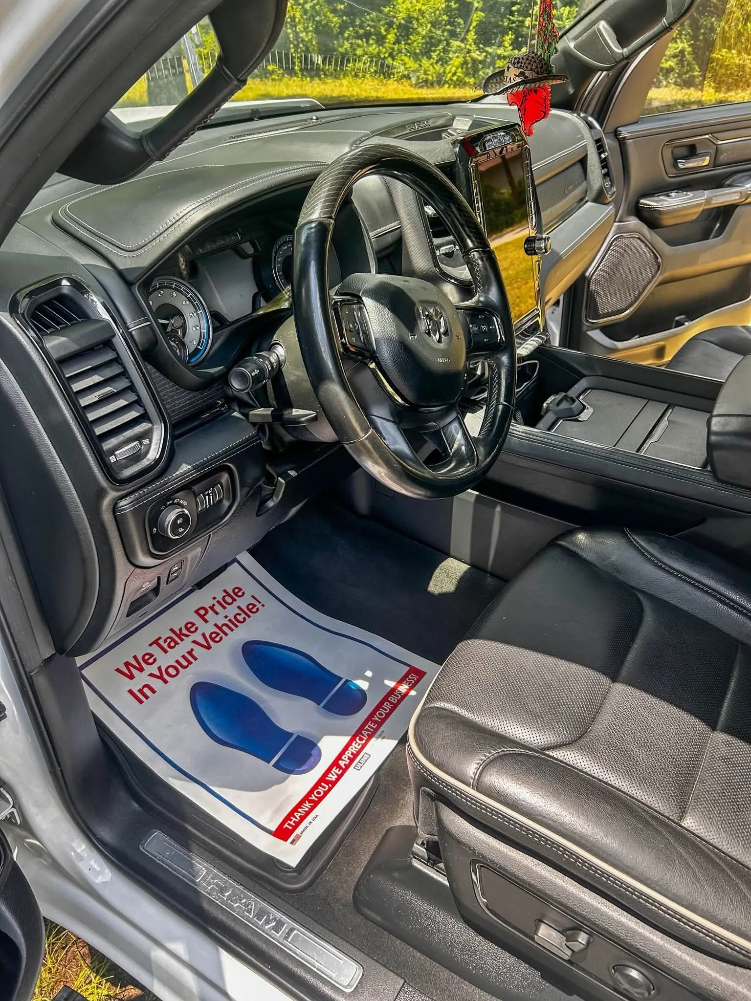 The interior of a vehicle showing the steering wheel, dashboard, and driver's seat with a floor mat that says 'Thank You. We Take Pride in Your Vehicle!'