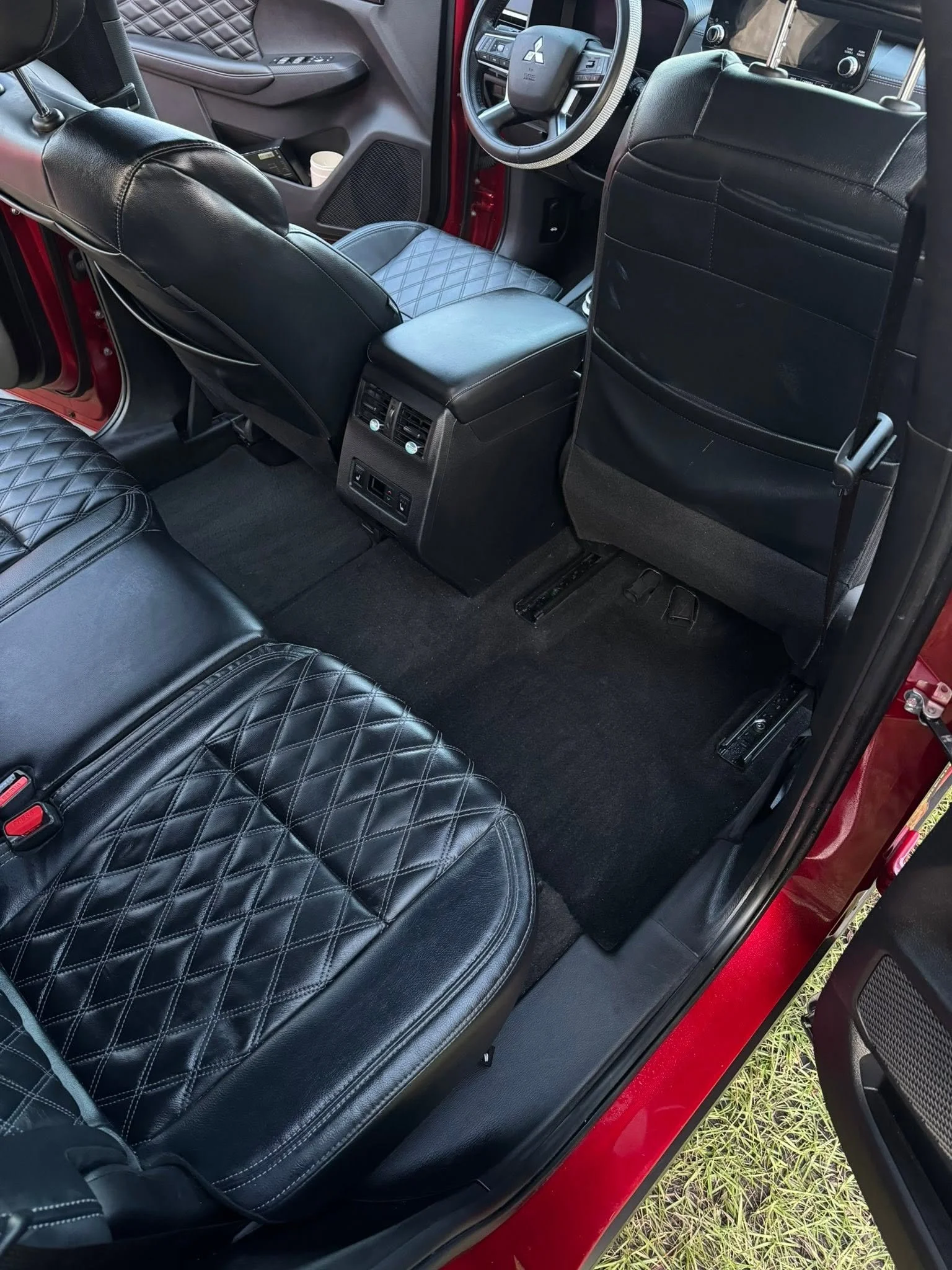 The interior of a vehicle showing black leather quilted seats, a dashboard with a steering wheel, and a backseat area with floor mats, door panels, and a center console with controls and vents.