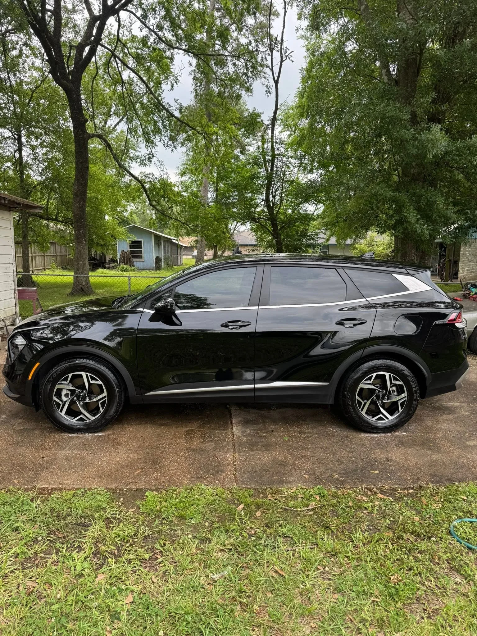 A black SUV parked on a wet driveway with green grass and trees in the background.
