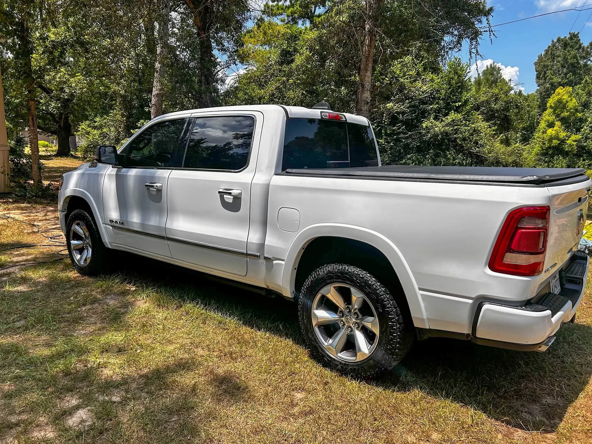 A white pickup truck parked on grass with trees and a blue sky in the background.