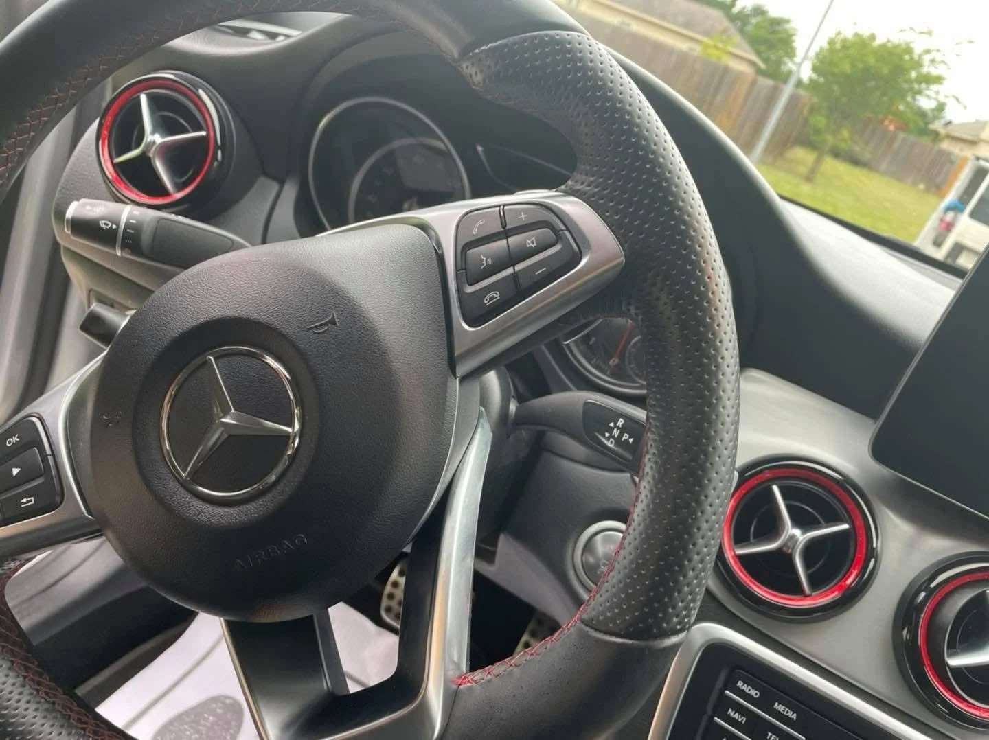 Interior of a Mercedes-Benz car showing the steering wheel, dashboard, and air vents with red accents.