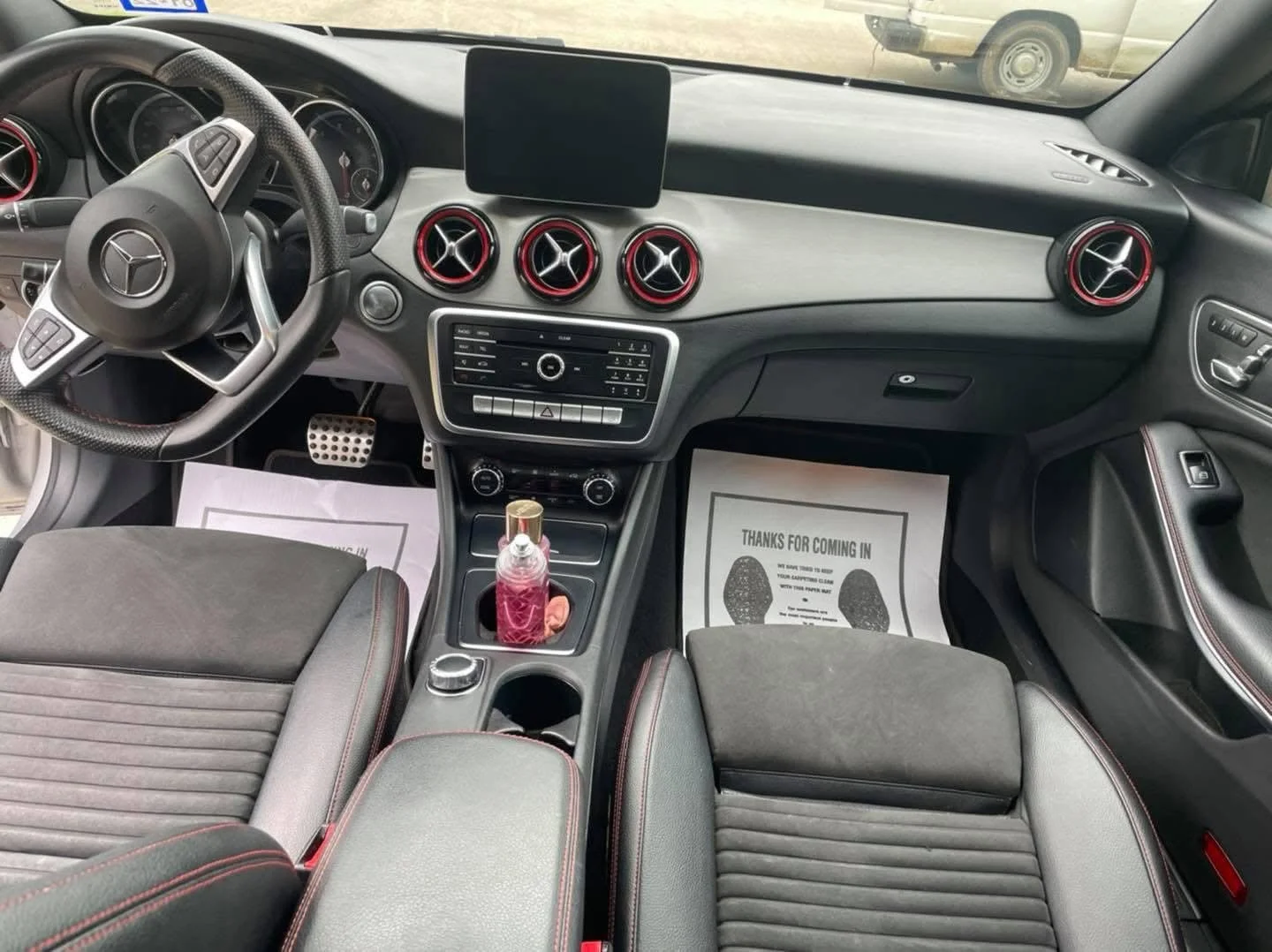 Interior of a car showing the dashboard, steering wheel, control panel, and front seats with a bottle in the center console.