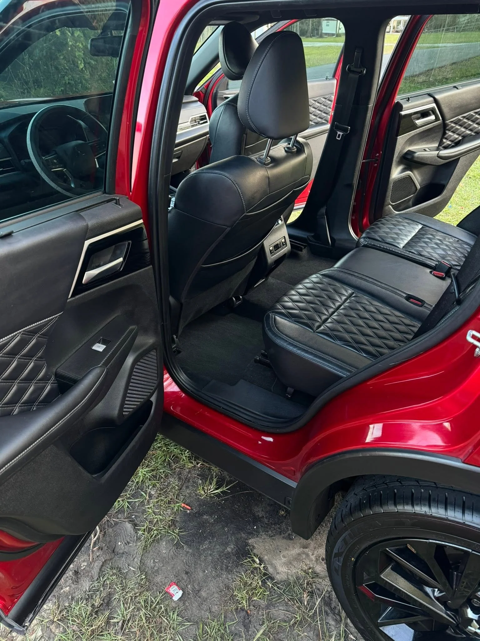 Interior of a red vehicle showing black leather seats with diamond quilting design, rear and front seats, black dashboard.
