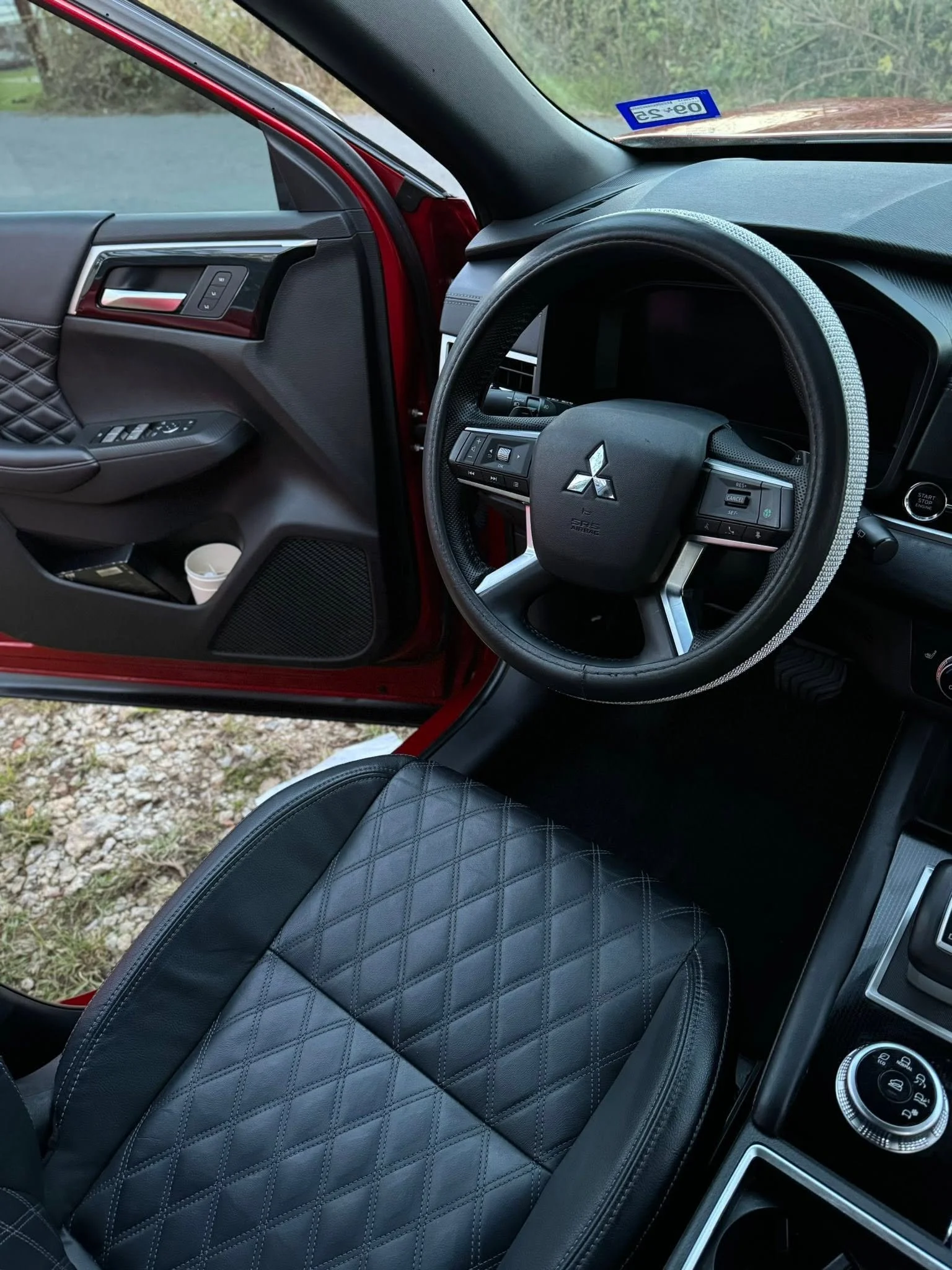 Inside view of a car showing the steering wheel, part of the dashboard, and a black quilted leather seat.