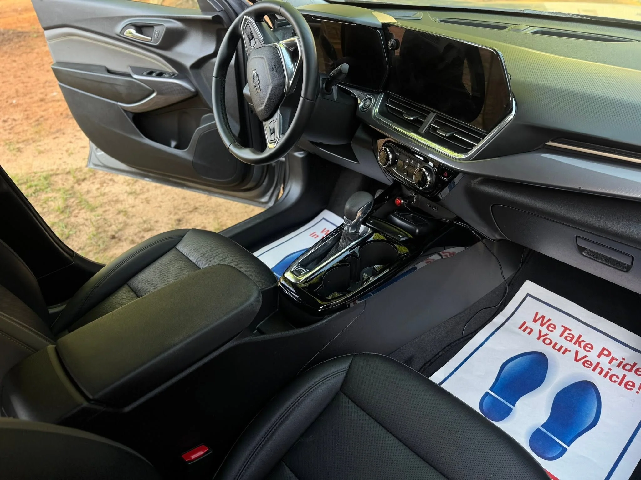 The interior of a gray Chevrolet vehicle showing the steering wheel, dashboard, center console, and part of the driver's seat. The dashboard includes an integrated digital display and air vents, with a paper with red and blue text and graphics on the