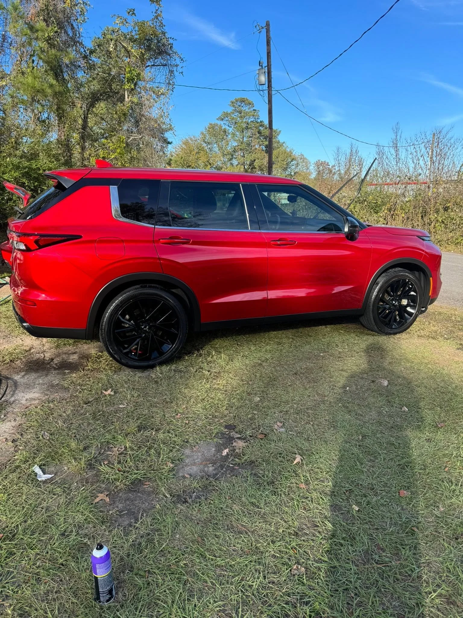 A red SUV parked on a grassy area with trees and a utility pole in the background. There is a spray can on the ground in the foreground.