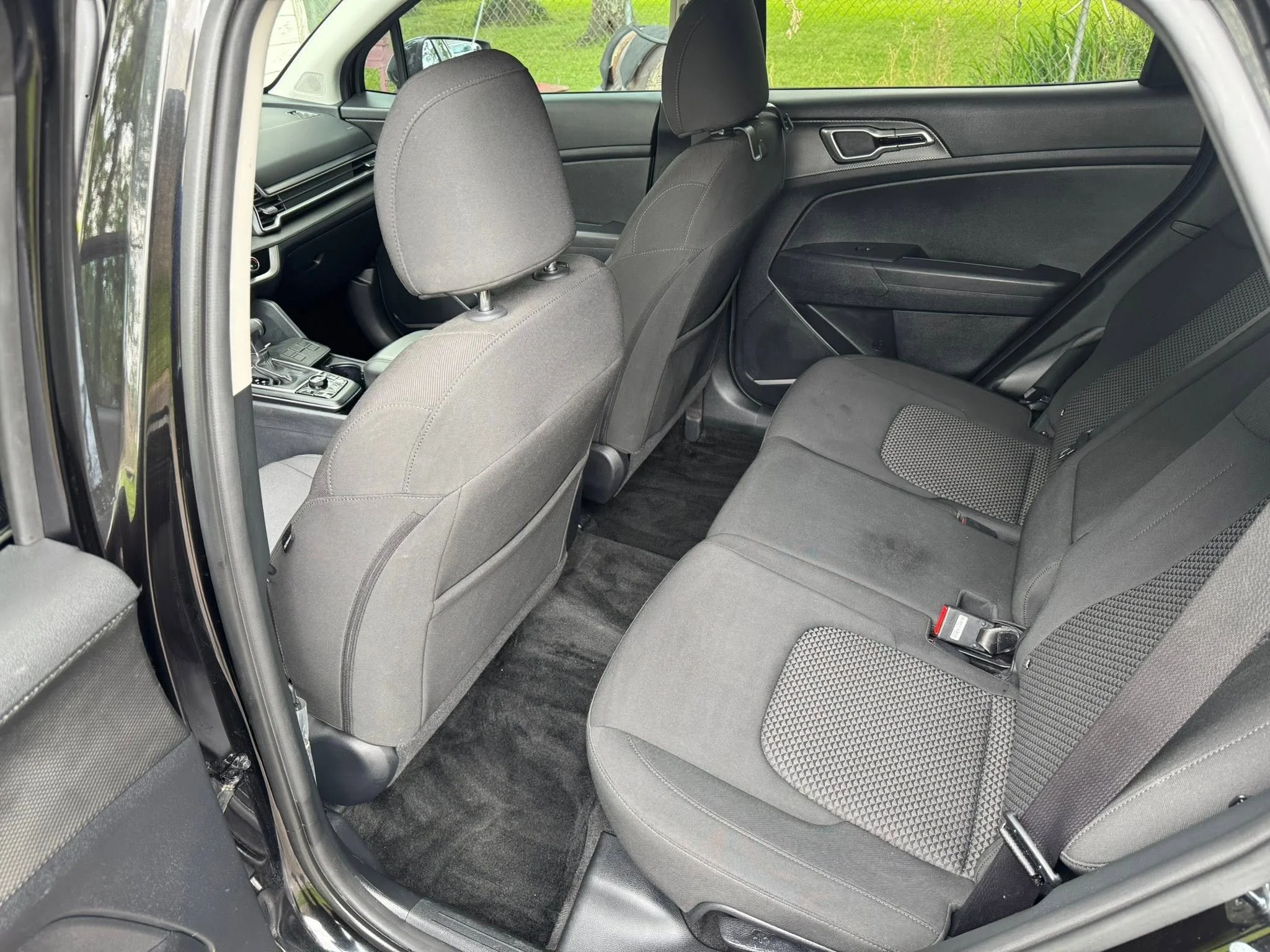 Interior of a modern car showing the back seats and part of the front seats, with gray fabric upholstery and black carpeting.