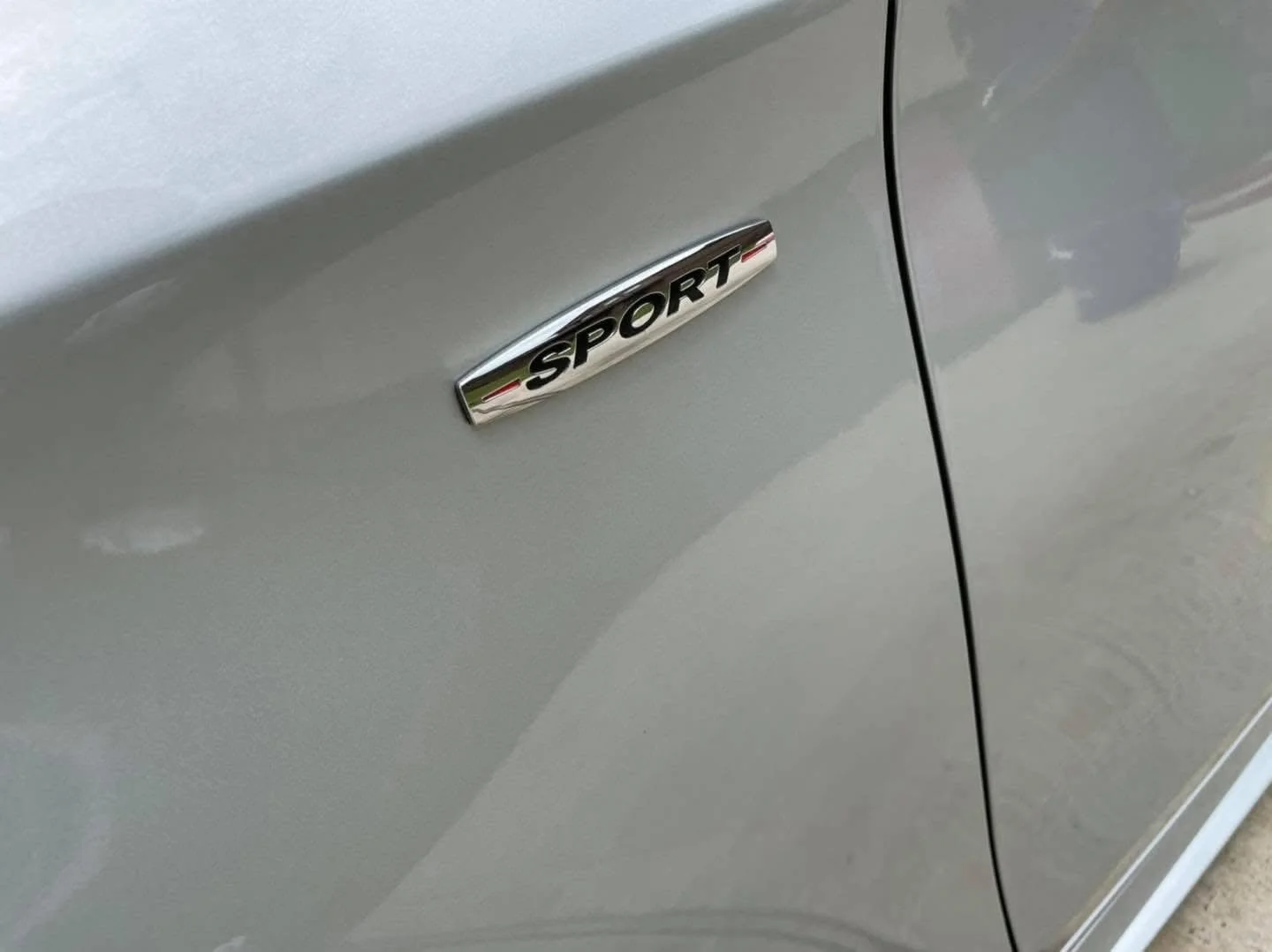 Close-up of a car's side displaying a chrome emblem with the word 'SPORT' on a silver vehicle.