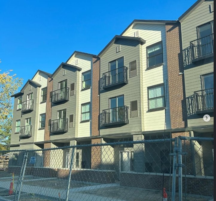 Modern multi-story residential building with balconies and a chain-link fence in front.