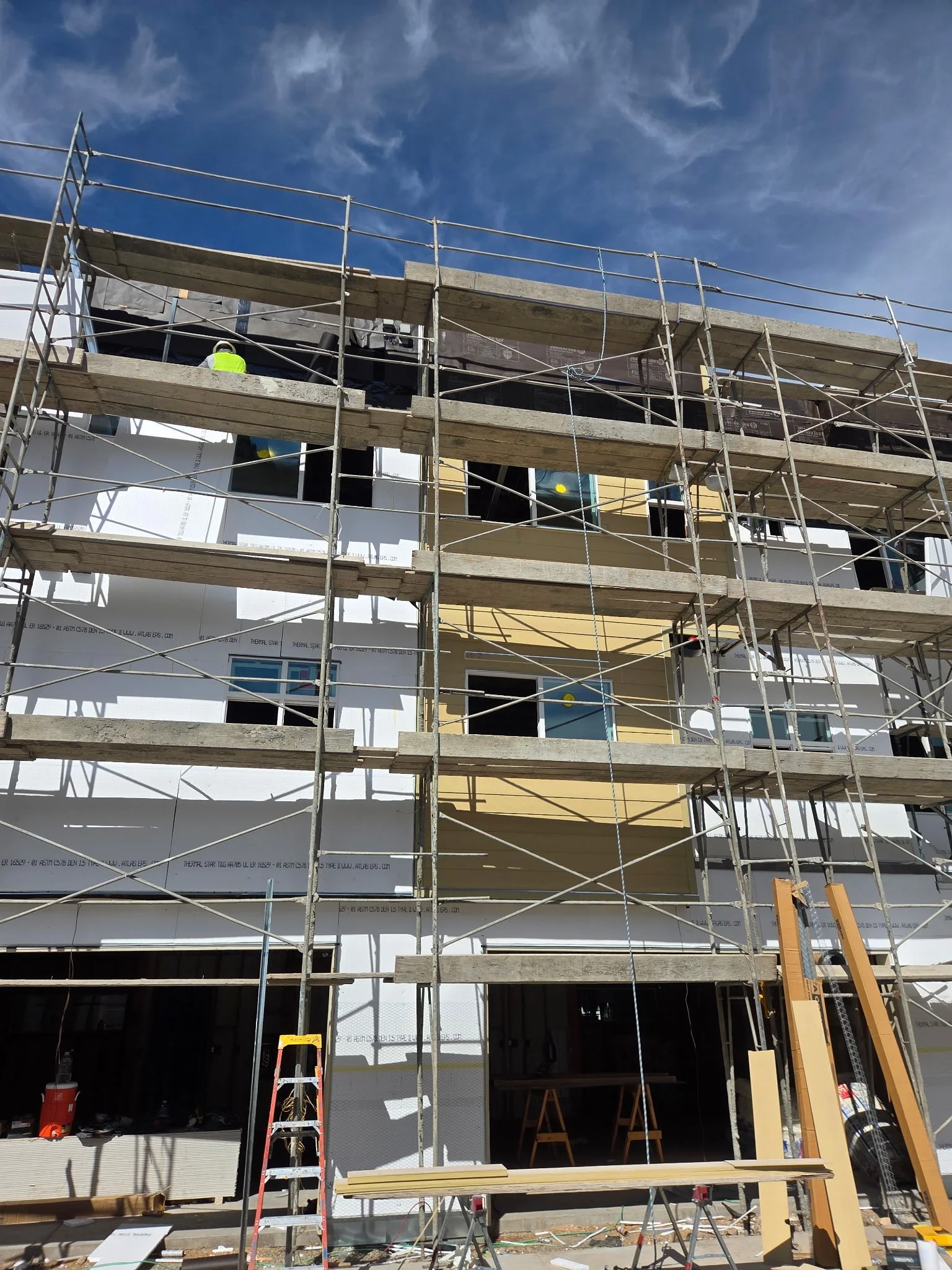 Construction site with scaffolding around a building under construction, with some open window spaces and building materials visible inside.