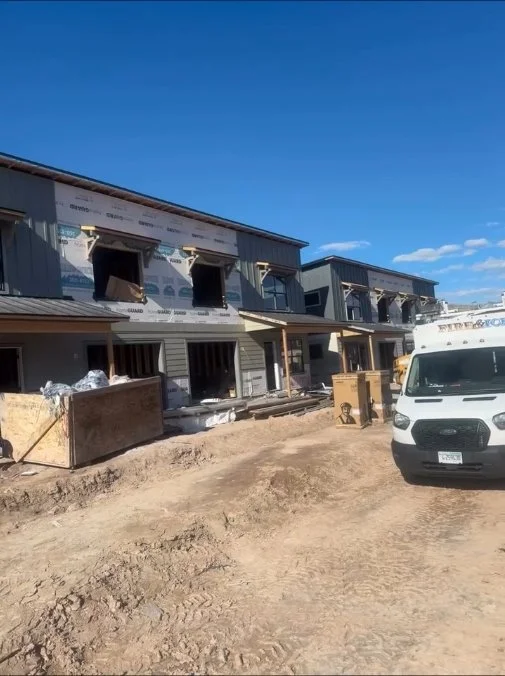 Construction site with partially built townhouses and a white utility van in the foreground under a blue sky.