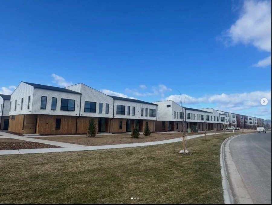 Modern row of townhouses with white and wood exteriors under a blue sky with clouds.