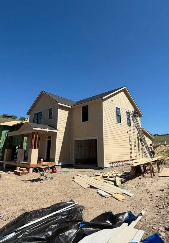 Under construction beige two-story house with scaffolding, ladder, and building materials around.