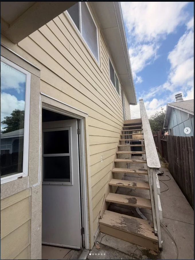 Backyard with new outdoor staircase unfinished, yellow siding house with white trim, dirt stairs, and partly cloudy sky.